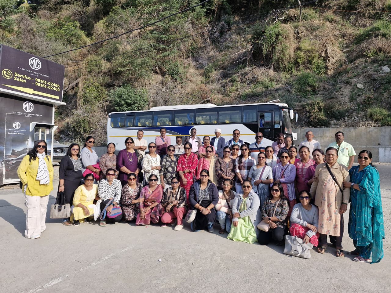 Group photo of people on a trip in front of bus and mountains